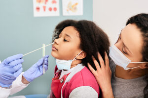 Little girl receiving a nasal swab test for COVID-19 in a medical lab with her mother