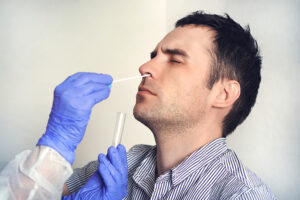Gloved hands of a medical practitioner insert a swab into the nose of young man