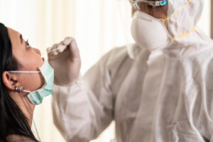 Medical professional in protective clothing and mask holds nasal swab, preparing to insert it into nose of young woman with uplifted face