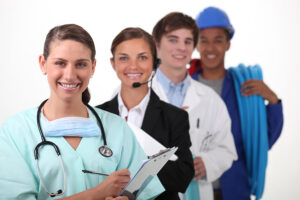 Young woman in medical scrubs with three other young adults dressed in different attire for various professions, including one in a hard hat