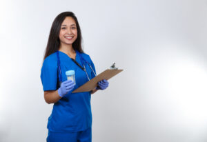 Smiling young woman in scrubs and gloves holds out an empty specimen bottle and holds a clipboard
