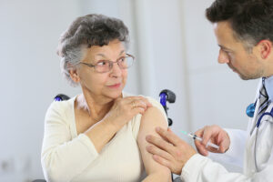 Senior woman with sleeve rolled up on her left arm gets a vaccine from a male doctor in a lab coat