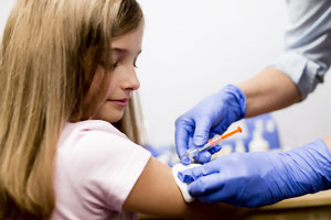 Grade-school-age girl gets a flu shot in her right arm from a technician wearing gloves