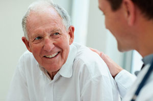 Senior male patient grinning at a young male medical professional shown from behind
