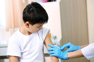 School-age boy looks at his arm as a medical practitioner's gloved hands prepare to inject a flu vaccine.