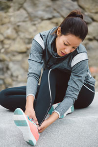 Young woman in jogging suit sits on the ground with right leg extended and examines her ankle