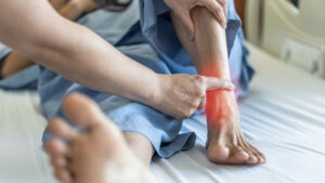 Detail shot of medical practitioner extending a hand and finger to press on a man's injured ankle 