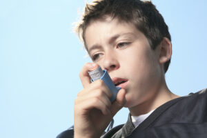 A male teen wearing football pads holds an asthma inhaler to his face