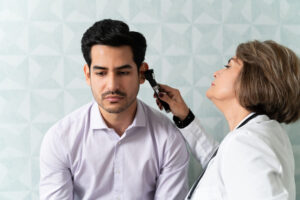 Caucasian female doctor examining male patient's ear with otoscope in hospital