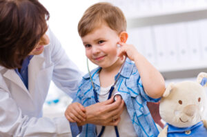 Senior female doctor examining happy young male child with stethoscope